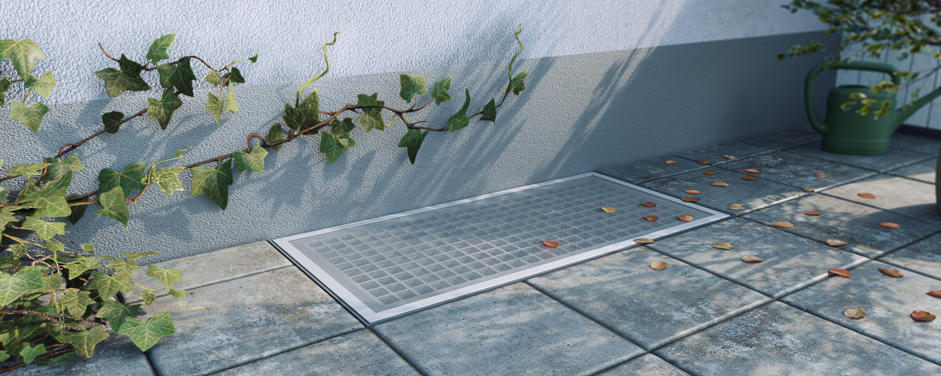 Silberne Lichtschachtabdeckung mit Blättern bedeckt, auf großen grauen Pflastersteinen