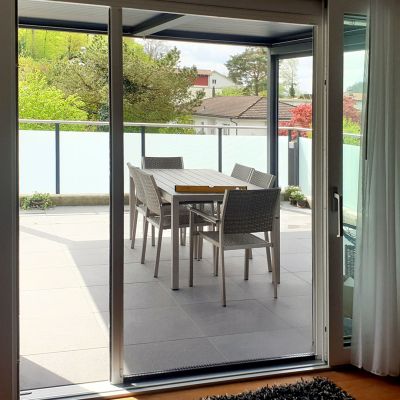 Fliegengitterrollotür leicht geöffnet. Draußen Terrassenmöbel