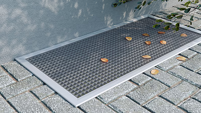 Silberne Lichtschachtabdeckung mit Blättern bedeckt, auf grauen Pflastersteinen