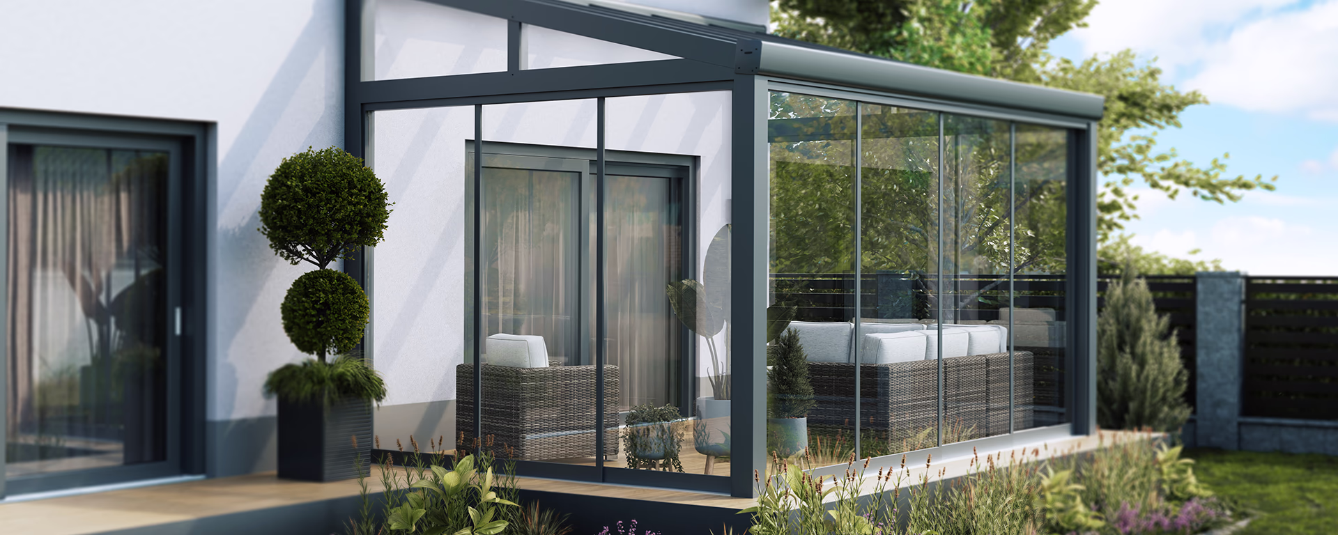 Anthraziter Wintergarten mit Gartenmöbeln und Pflanzen vor weißer Hauswand