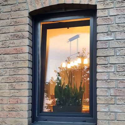 Fliegengitterspannrahmen am gekippten Fenster. Innen brennt Licht