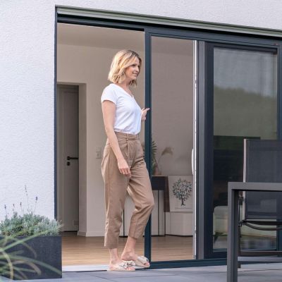 Frau steht an geöffneter Fliegengitter-Schiebetür